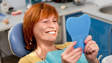 Patient looking at her dental implants in a mirror and smiling