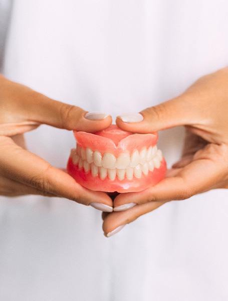 Hands holding complete set of dentures in front of white-clothed midsection