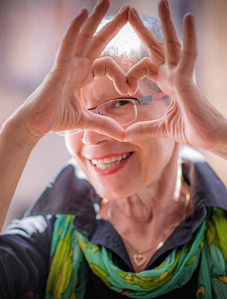 Woman in green scarf smiling and making a heart shape with her fingers around her eye