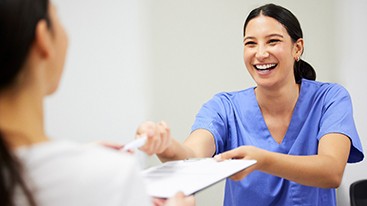 Smiling dental assistant handing patient form
