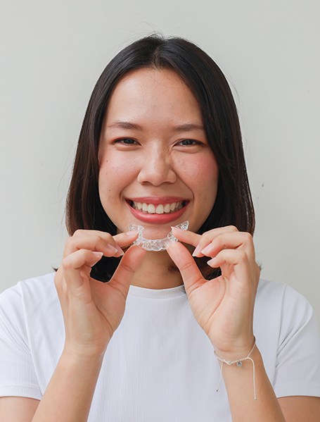 Woman smiling while holding clear aligner
