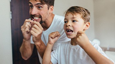 Father and son flossing teeth together in bathroom