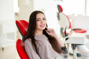 Woman smiling in dental chair after receiving cosmetic dental treatment